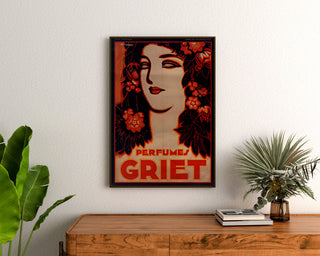 Vintage reclameposter Perfumes Griet, ingelijst boven een houten dressoir, tussen planten.