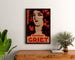 Vintage reclameposter Perfumes Griet, ingelijst boven een houten dressoir, tussen planten.
