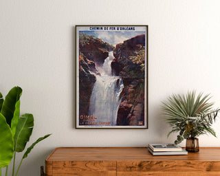 Vintage toeristische poster – Gimel, la Grande Cascade, ingelijst boven een houten dressoir tussen planten.