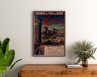 Vintage affiche Coucy, Chemins de Fer du Nord, ingelijst boven een houten dressoir, tussen planten.