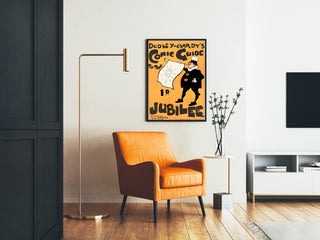Vintageposter Dudley Hardy, comic guide, ingelijst in een woonkamer met een oranje fauteuil en een leeslamp.