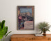 Vintage Lourdes seaside poster, framed above a wooden dresser, between plants.