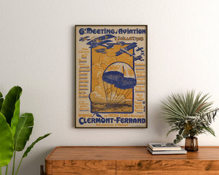 Vintage poster Meeting d’aviation, Clermont-Ferrand, ingelijst boven een houten dressoir, tussen planten.