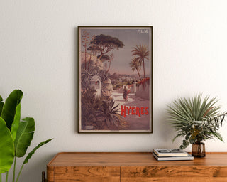 Vintage poster P. L. M. Hyères, ingelijst boven een houten dressoir, tussen planten.