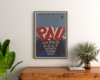 Vintageposter Pau, golf et sports, ingelijst boven een houten ladekast tussen planten.