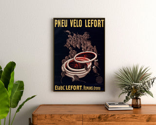 Vintage poster Lefort bicycle tires, framed above a wooden dresser between plants.