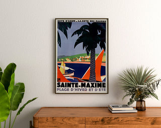 Vintage poster Sainte-Maxime, Côte des Maures, ingelijst boven een houten dressoir, tussen planten.